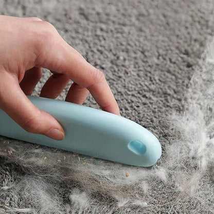 Handheld pet hair scraper brush pulling a pile of dog fur out of a carpet