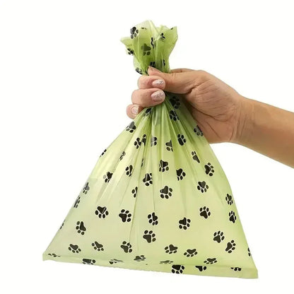 Hand holding a tied green paw-print dog poop bag