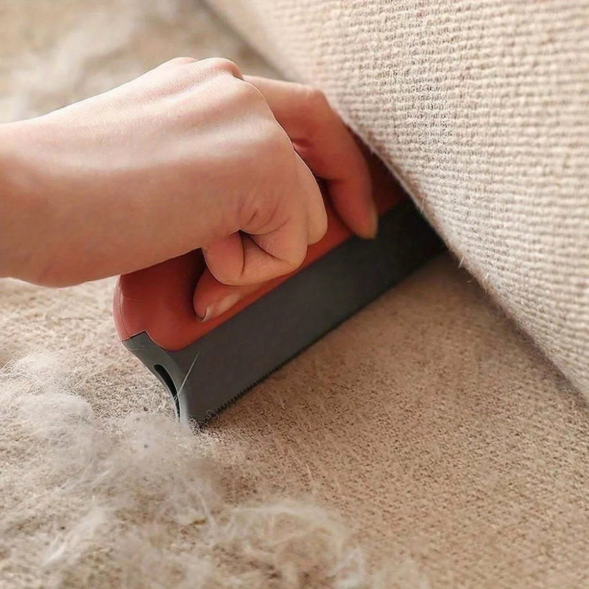 Handheld pet hair scraper brush pulling a pile of dog fur out of a carpet