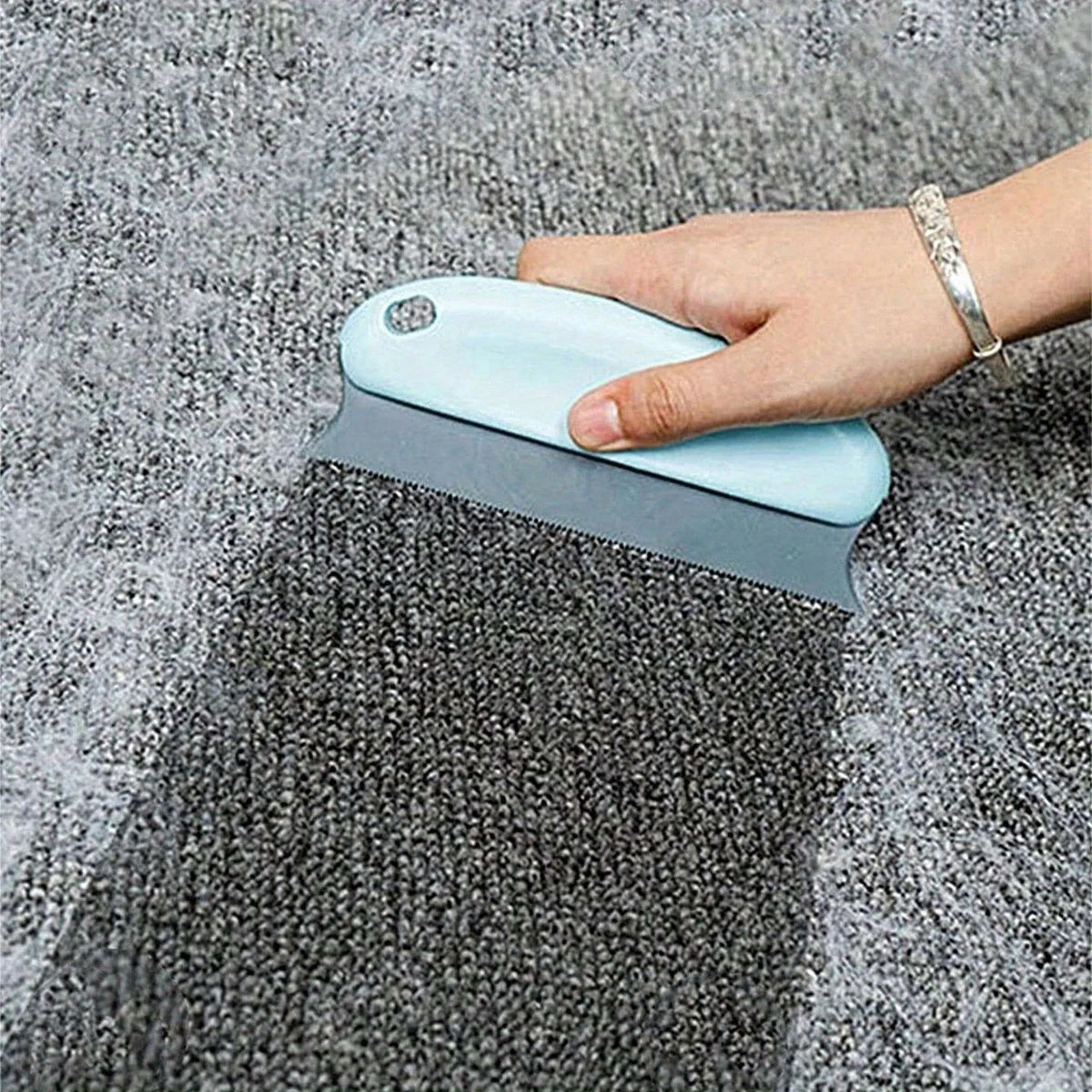 Handheld pet hair scraper brush pulling a pile of dog fur out of a carpet